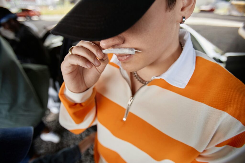 Close-up of young man in black cap and striped pullover holding joint by nose