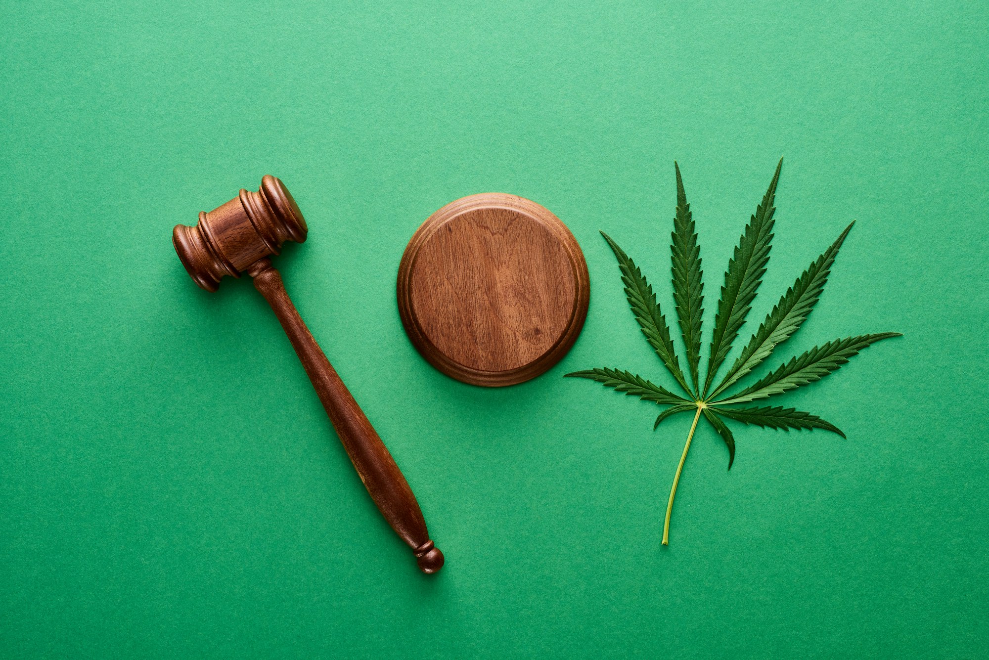 top view of green marijuana leaf with wooden gavel on green background