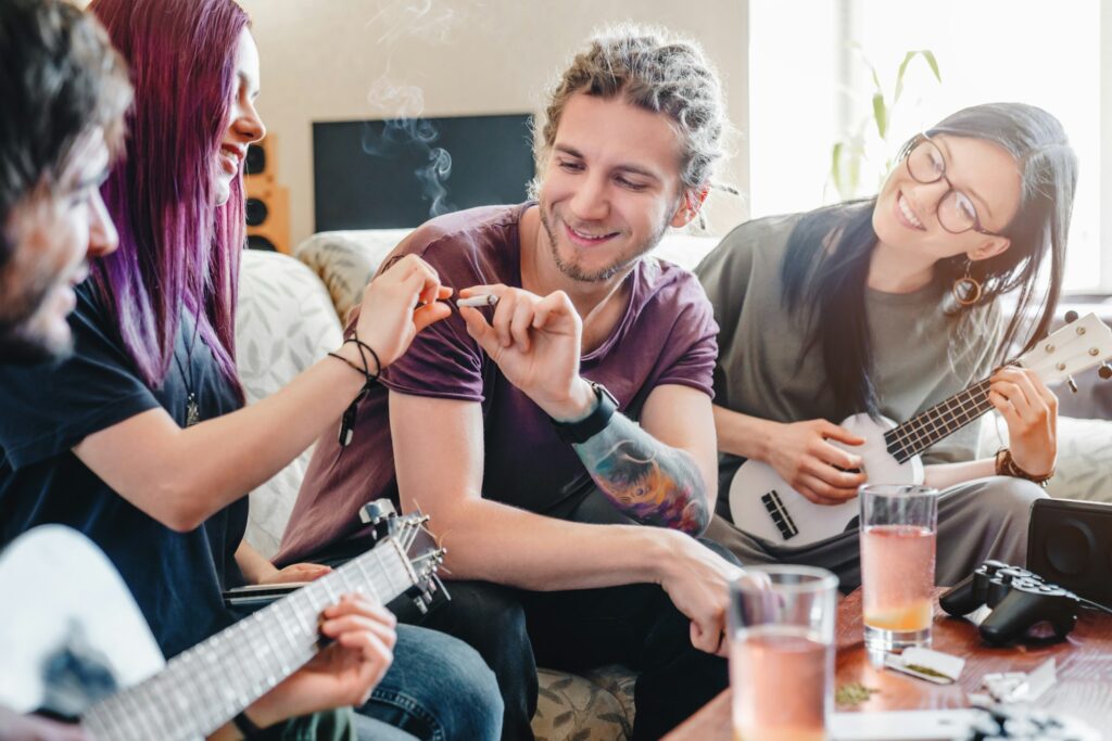 Young man going to smoke joint rolled with cannabis while relaxing with friends at home