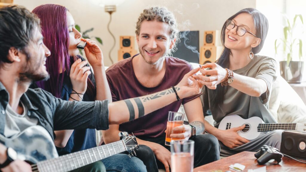 Young woman preparing to smoke joint with cannabis while relaxing with friends at home